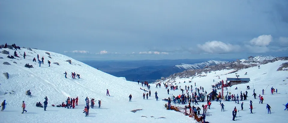 Visitantes y pistas nevadas en la parte alta del Cerro Catedral, con montañas al fondo.